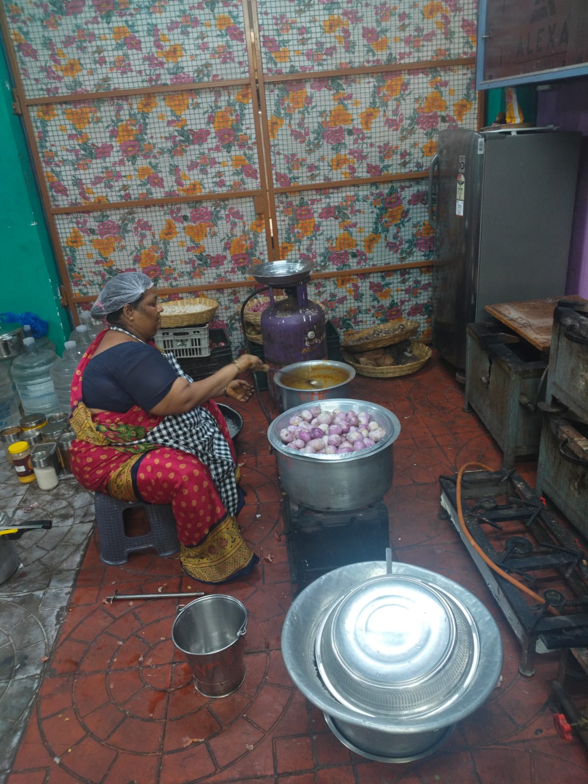Traditional Tamil cook preparing fresh sambar with peeled baby onions on commercial stove